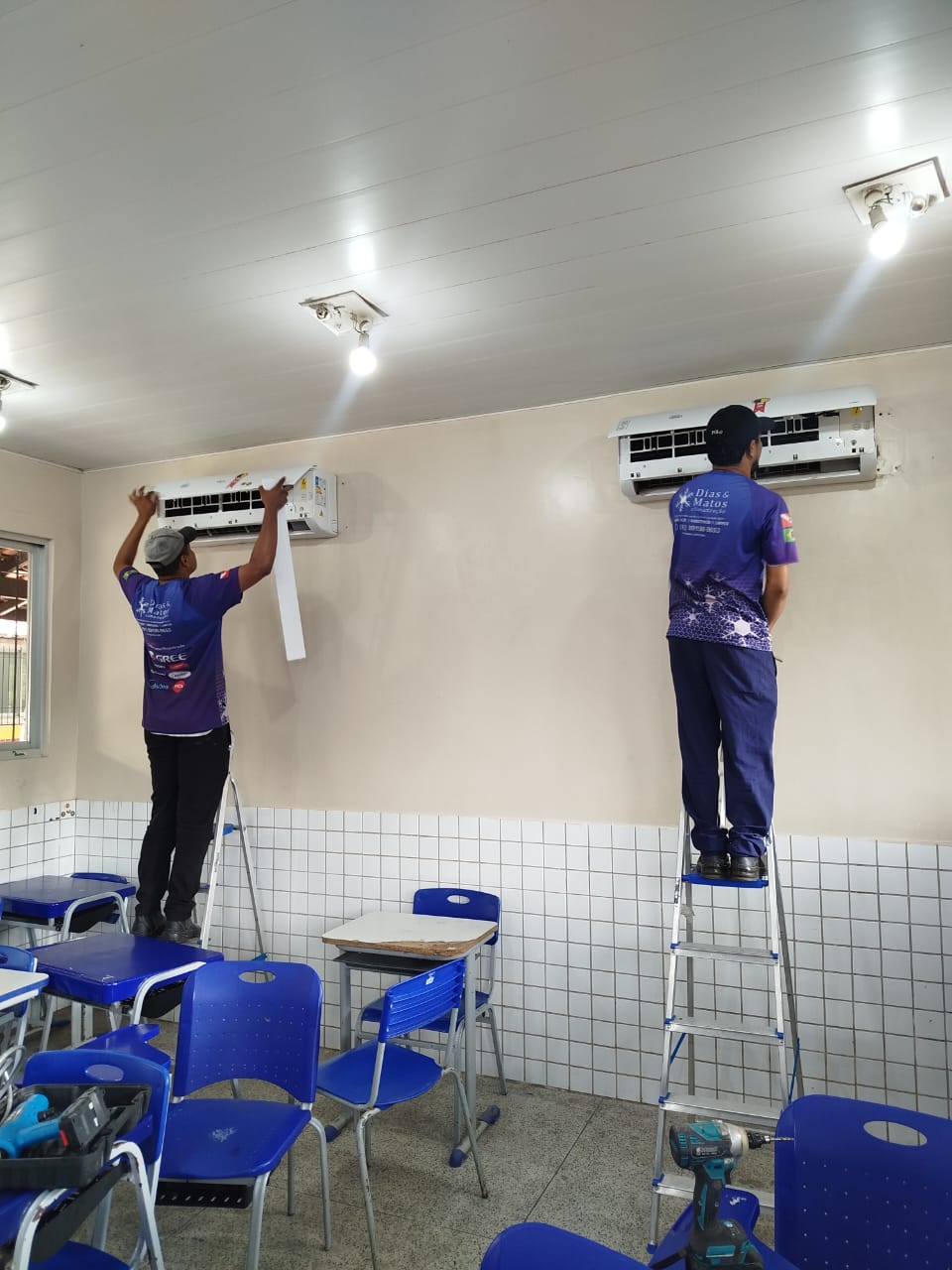Dois técnicos uniformizados da Dias & Matos realizando serviço em aparelhos de ar-condicionado split em uma sala