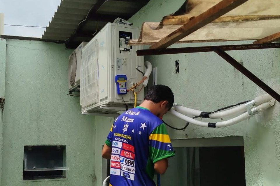 Técnico uniformizado sobre escada trabalhando junto à unidade externa do split no Condomínio Jardim Espanha